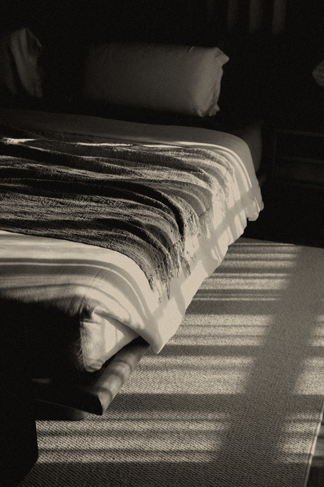 A sunlit bed corner with a woven throw